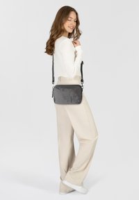 Bolso cruzado negro texturizado con cierre de cremallera y correa ajustable, con un sutil logotipo en la parte frontal.