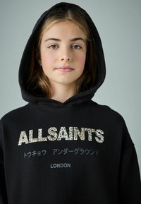 Čierna mikina s kapucňou s nápisom "ALLSAINTS" v leopardom vzore, doplnená o text v japončine a "LONDON" v bielej farbe. Hladká textúra látky.