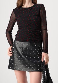 Svart långärmad topp med röda hjärtmönster, skräddarsydd design. Kombinerad med en svart lädernederdel med silverfärgade nitar.