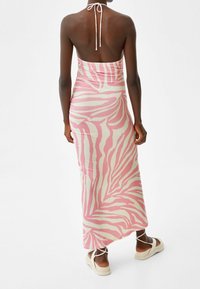 Maxikleid aus leichtem Stoff mit pink-weißen Zebramustern, ausgestattet mit einem Rückengurt und einer figurbetonten Silhouette, kombiniert mit hellen Sandalen.