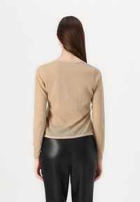 Langærmet guld, gennemsigtig sweater med rund halsudskæring, struktureret strik og tætsiddende pasform, parret med sorte bukser i faux læder.