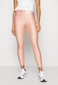 Leggings sportivi rosa con righe verticali, dotati di una vita alta e una texture liscia e lucida. Abbinati a scarpe da corsa bianche.