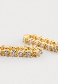 Guldtonede øreringe med en række klare ædelstene, med et tekstureret design og afrundede accentformer. Elegant og funkende visuel detalje.