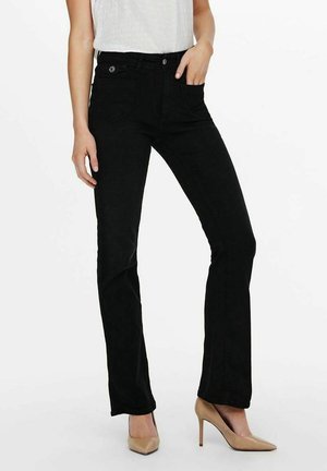 Vrouw draagt zwarte, recht gesneden jeans met hoge taille en voor- en zijkanten zakken, gecombineerd met naakte, puntige hoge hakken en een witte blouse, ingestopt.