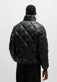 Giacca invernale nera trapuntata con colletto alto, dotata di un piccolo logo sul retro, polsini elastici e una texture liscia e lucida.
