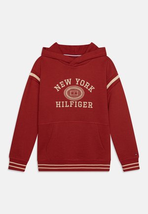Sweat à capuche rouge avec des bandes beiges sur les manches et l'ourlet, poche avant, et texte « New York Hilfiger » avec logo sur la poitrine.