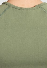 Olijfgroene getailleerde shirt met een gladde, gestructureerde stof, een ronde halslijn en zichtbare naaddetails. Het ontwerp is eenvoudig en modern.