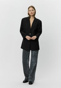 Sacou oversized negru, cu un singur nasture, asortat cu pantaloni gri cu print de panteră, evazați, și pantofi negri lucioși.