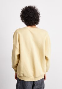 Žuta sweatshirt s opuštenim krojem i spuštenim ramenima. Ima rebraste manžete i rub. Upairana s sivim, širokim hlačama.