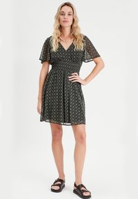 Schwarz-blumiges Kleid mit kurzen, schwingenden Ärmeln, tailliertem Bund und ausgestelltem Rock. Getragen mit schwarzen Sandalen.