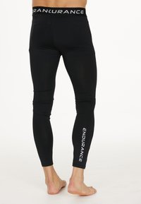 Leggings de sport noirs avec une texture lisse, dotés d'une large ceinture ornée du mot "ENDURANCE" et d'un design longueur cheville.