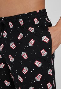 Pijamas negros con un patrón de palomitas de maíz, con cajas de palomitas a rayas rojas y blancas, cinturilla elástica y bolsillos laterales.