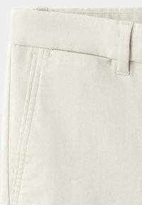 Gros plan de la partie supérieure d’un pantalon écru montrant la ceinture, la boucle de ceinture et la couture latérale.