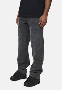 Jeans in denim grigio con una vestibilità rilassata, caratterizzati da un design a gamba dritta e una texture sbiadita. Indossati con sneakers nere, che mostrano un look casual.