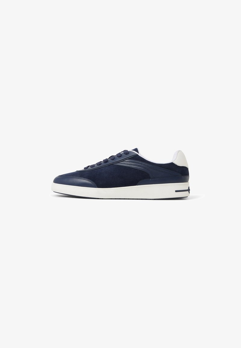 Zapatillas de ante en color marino con suela de goma blanca. Presentan punta redondeada, diseño de cordones y acentos laterales texturizados. Estilo minimalista.