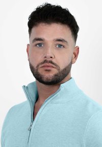 Lichtblauwe ritsvest gemaakt van zacht materiaal, met een geribde kraag en subtiele textuur, weergegeven op een persoon tegen een effen achtergrond.