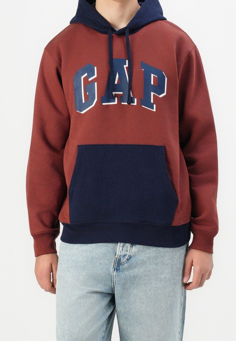 Viininpunainen ja tummansininen huppari, jossa on etutasku, kiristysnauha hupussa ja "GAP"-logo vahvoissa, kontrastoivissa väreissä. Puuvillasekoitekangas.