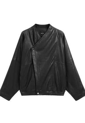 Giacca in pelle nera con texture, maniche larghe, chiusura frontale asimmetrica con bottoni a pressione e cuciture ben visibili.