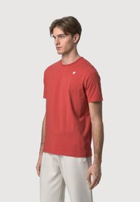 T-shirt in cotone rosso con scollatura rotonda, maniche corte e un piccolo logo bianco sul lato sinistro. Tessuto morbido, design aderente.