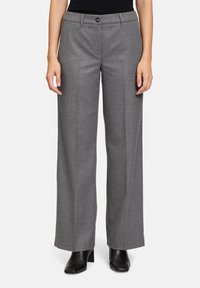 Pantalons ajustés gris avec une coupe droite, fermeture à bouton et zip à l'avant, fabriqués en tissu texturé. Portés avec des chaussures noires.