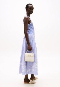 Abito a righe blu e bianche con top attillato e fondo svasato. Tieni una piccola borsa bianca con una finitura dorata. Ballerine beige intrecciate.