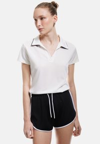 Witte polo met kraag en zwarte accenten, gecombineerd met zwarte shorts met witte zijkanten en een drawstring taille. Gladde stofstructuur.