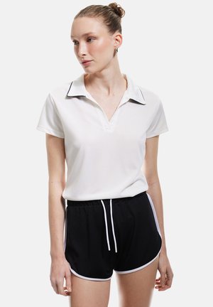Witte polo met kraag en zwarte accenten, gecombineerd met zwarte shorts met witte zijkanten en een drawstring taille. Gladde stofstructuur.