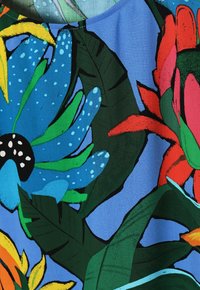 Blumenstoff mit blauem Hintergrund, der lebendige grüne Blätter, große blaue Blumen mit schwarzen Zentren und rote Akzente zeigt.