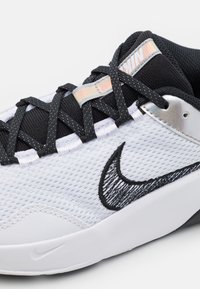 Biały siateczkowy sneaker z czarnymi akcentami, teksturowanymi sznurowadłami i srebrnym panelem na pięcie. Na boku wyraźne czarne logo Nike swoosh.