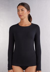 Schwarzes langärmliges Shirt aus leichtem Stoff mit Rundhalsausschnitt und figurbetontem Schnitt, das eine glatte Textur aufweist.