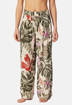 Loose-fitting pants with elastic waistband featuring large green leaves, red and pink tropical floral print, worn barefoot on light background.