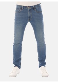 Ljust blå denimjeans med smal passform och femficksdesign. Funktionen inkluderar sydda detaljer, knäppning med knapp och bälteshällor. Bärs med vita sneakers.