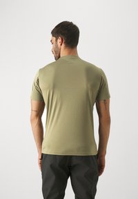Camiseta de manga corta verde olivo hecha de tejido suave, con cuello redondo y diseño ajustado, combinada con pantalones oscuros y ajustados.