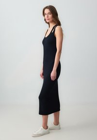 Robe midi noire avec une coupe ajustée, dotée d'un motif checkered texturé et de découpes aux épaules. Portée avec des baskets blanches.