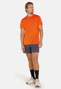 Orange kortærmet T-shirt parret med mørkegrå shorts, båret med sorte knæhøje sokker og lyse sportsko.