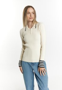 Crème gekrulde long-sleeve polo met een twee-knops sluiting en marineblauwe en witte gestreepte manchetten, gecombineerd met lichtblauwe denim jeans.