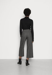 Czarny sweter w golf z długimi rękawami w połączeniu z szarymi spodniami o szerokiej nogawce. Osoba nosi czarne botki za kostkę. Prosty, elegancki design.