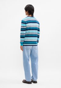 Pull multicolore à rayures horizontales dans des nuances de bleu, avec un col rond et des poignets côtelés, associé à un jean décontracté bleu clair.