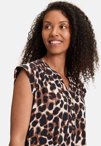 Blusa a maniche corte con stampa leopardata in marrone, beige e nero. Tessuto leggero con apertura frontale a bottoni e spalle plissettate.