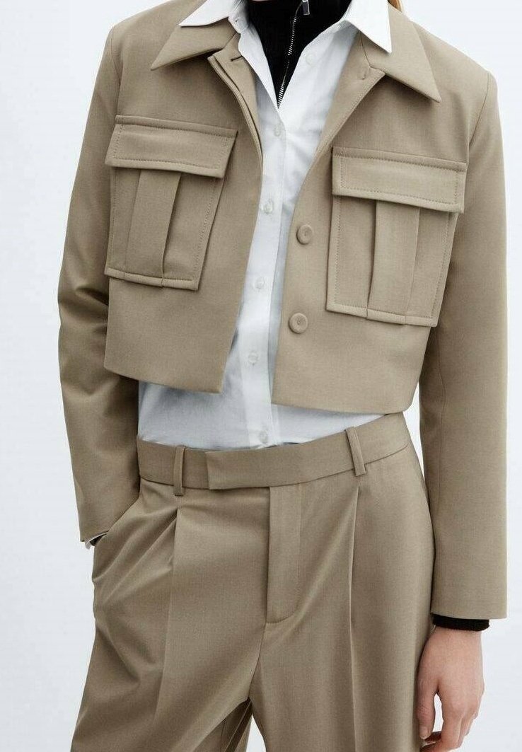 Veste beige cropped avec deux poches avant, assortie à une chemise blanche et un pantalon taille haute beige. Tissu lisse et design structuré.