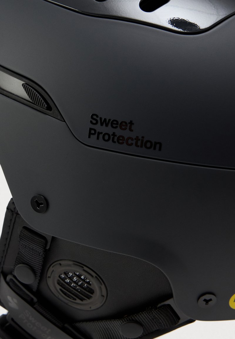 Schwarzer Helm mit mattem Finish, Belüftungsöffnungen und verstellbarem Riemen. Enthält das geprägte Logo "Sweet Protection" und auffällige Hardware-Akzente.