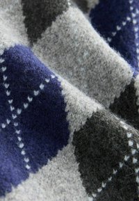Wollstoff mit einem Diamantmuster in marineblau, grau und schwarz; weiche Textur mit sichtbarem Fussel und weißen Stichakzenten.