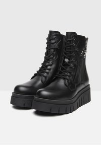 Bottines en cuir noir avec fermeture à lacets à l'avant et zip latéral. Semelle épaisse en plateforme avec des rainures profondes. Texture lisse, design minimaliste.