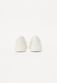 Hvide sneakers med en tekstureret læderoverdel, rund tå og en tyk gummisål. Bagfra ses en glat finish og polstret krave.
