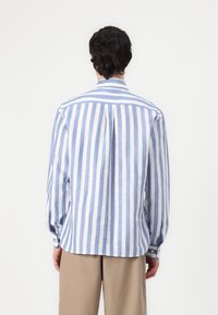 Camicia a maniche lunghe con righe verticali blu e bianche, colletto e polsini con bottoni. Tessuto leggero con vestibilità rilassata.