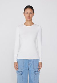 Weißes Langarm-T-Shirt mit Rundhalsausschnitt, enganliegendem Design, glatter Textur und minimalen Nähten, kombiniert mit hellblauen oversize Cargo-Jeans.