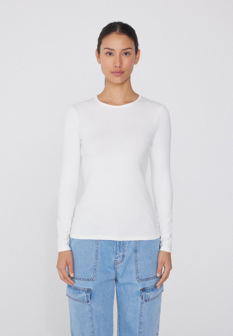 Weißes Langarm-T-Shirt mit Rundhalsausschnitt, enganliegendem Design, glatter Textur und minimalen Nähten, kombiniert mit hellblauen oversize Cargo-Jeans.