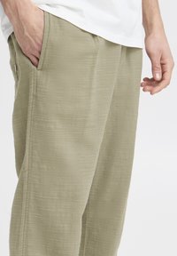Light green, textured trousers with side pockets and a relaxed fit. Fabric appears soft and slightly wrinkled, adding visual interest.