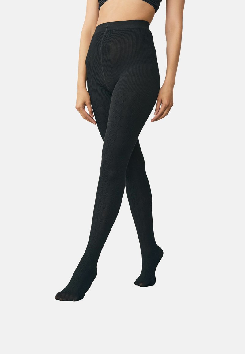 Schwarze gerippte Strumpfhosen mit hohem Bund. Der Stoff weist ein strukturiertes Muster auf. Sie sind knöchellang und haben Füße, mit einem engen Sitz über die gesamte Länge.
