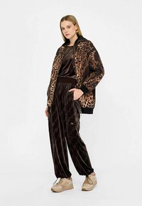 Pruun sametist dressipluus leopardimustrilise jakiga, millel on ees lukk, soonikkoes varrukasääred ja pükstel logo detailid. Helebeežid spordijalatsid.